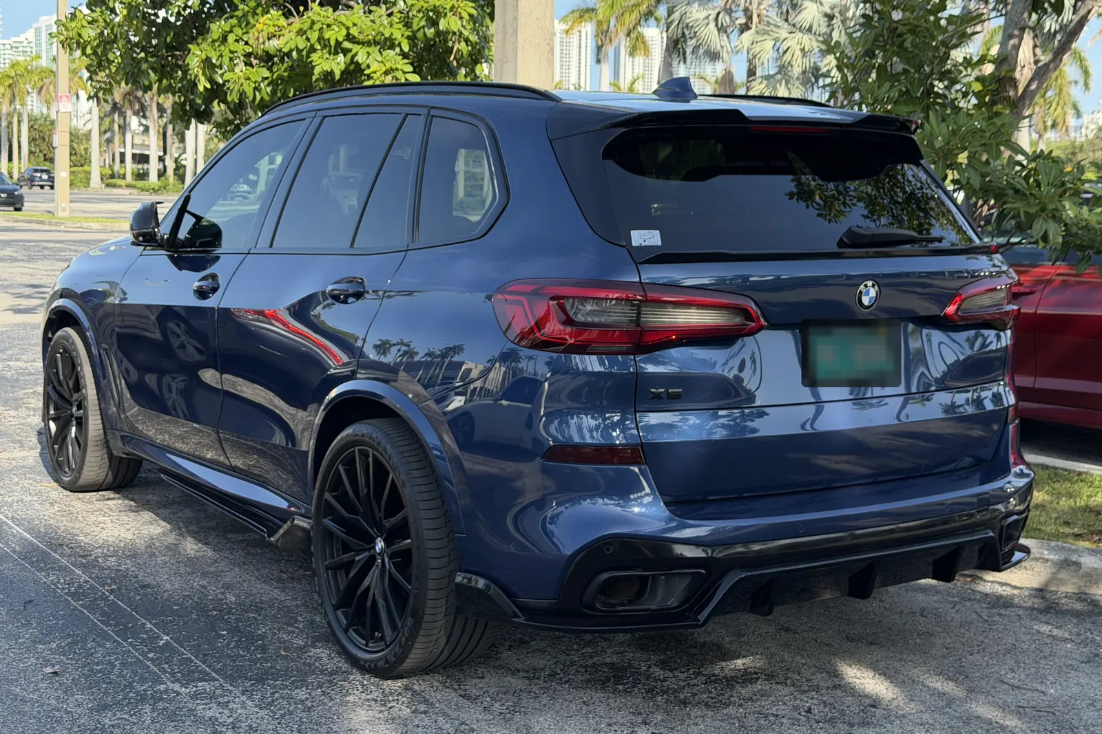 Dark blue BMW X5 from the rear three-quarter, palm trees reflected in the paint